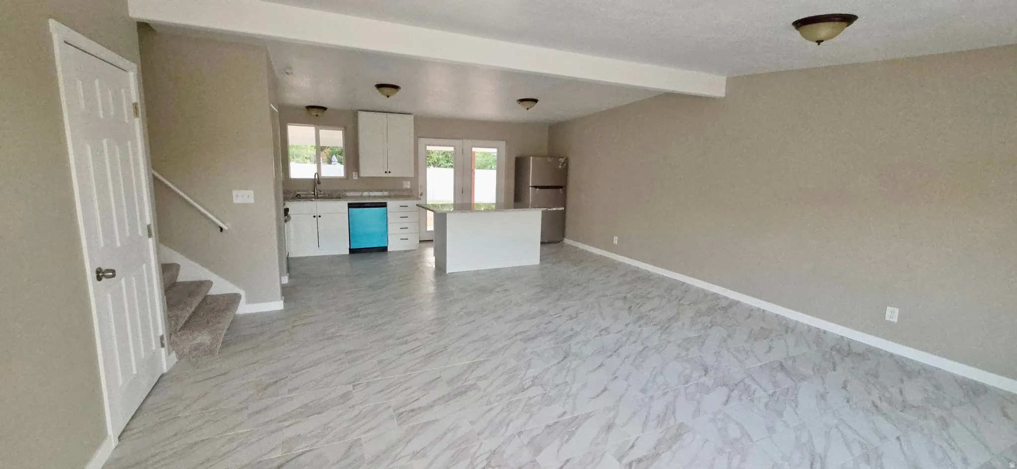 Open-concept living space with light-toned walls, overhead lighting fixtures, and light-toned tile flooring