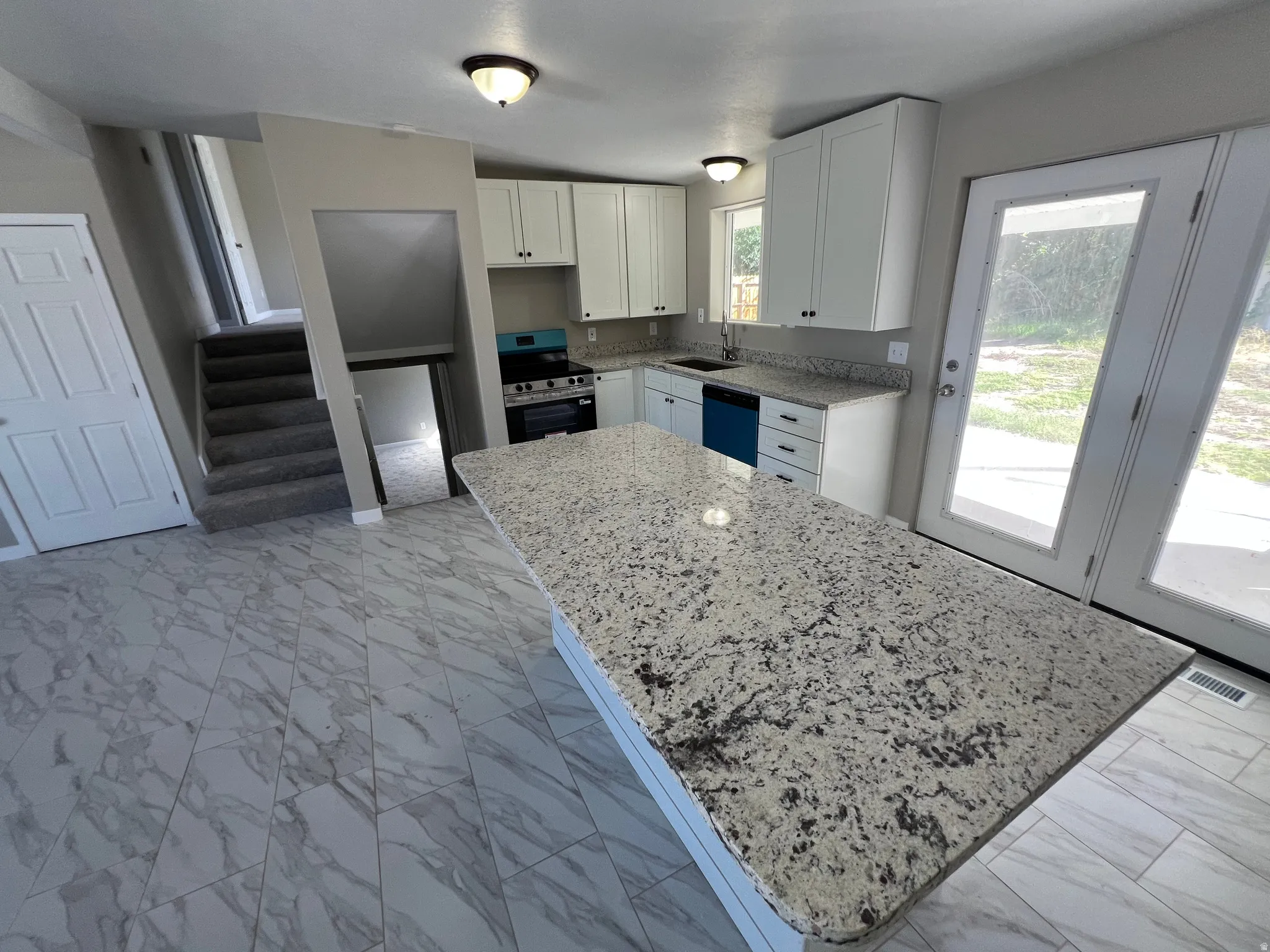 Kitchen island with a granite countertop, white cabinetry with black hardware, stainless steel range, and a dual-basin sink