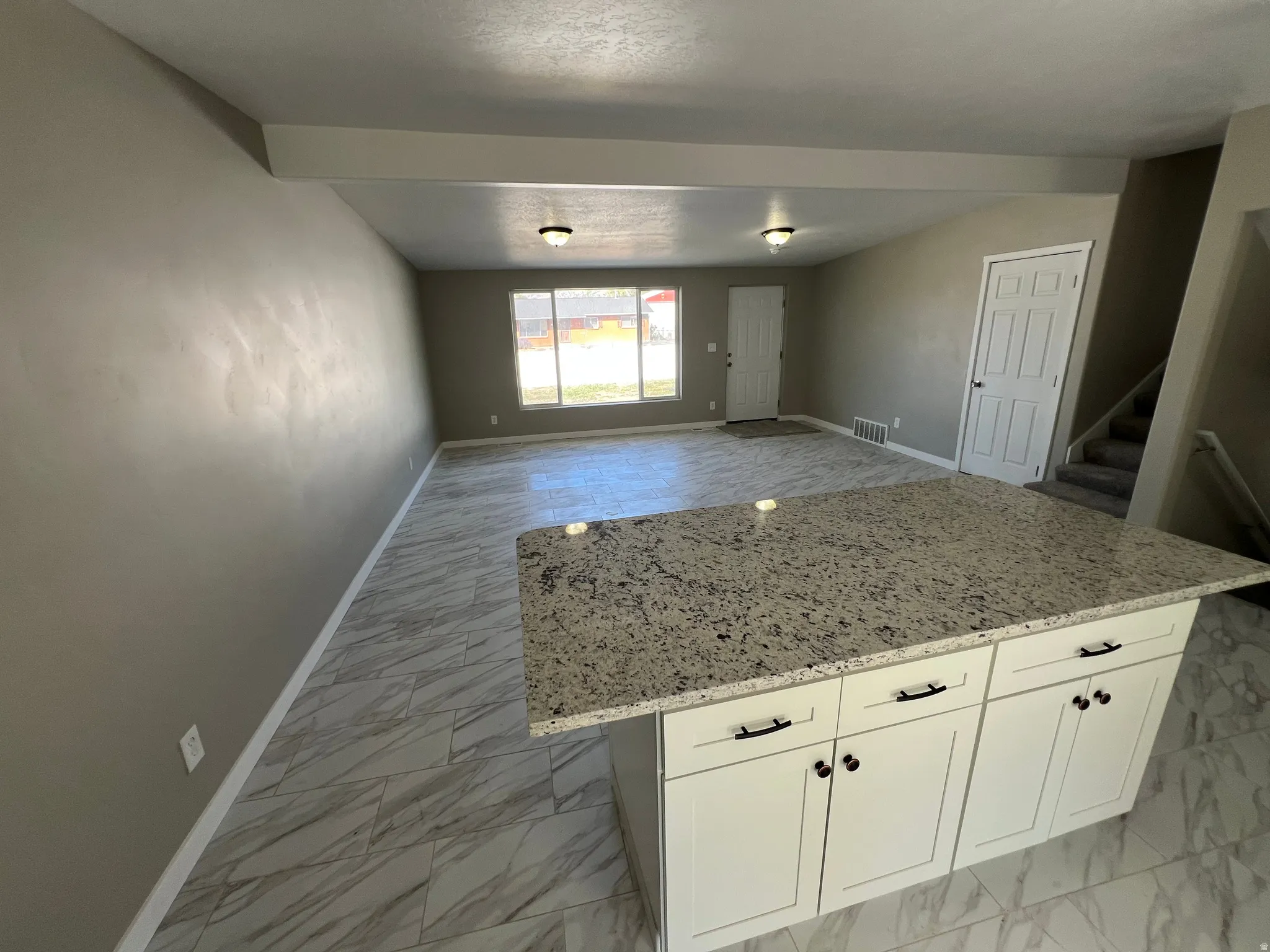 Kitchen island with a light-toned granite countertop and white shaker-style cabinetry