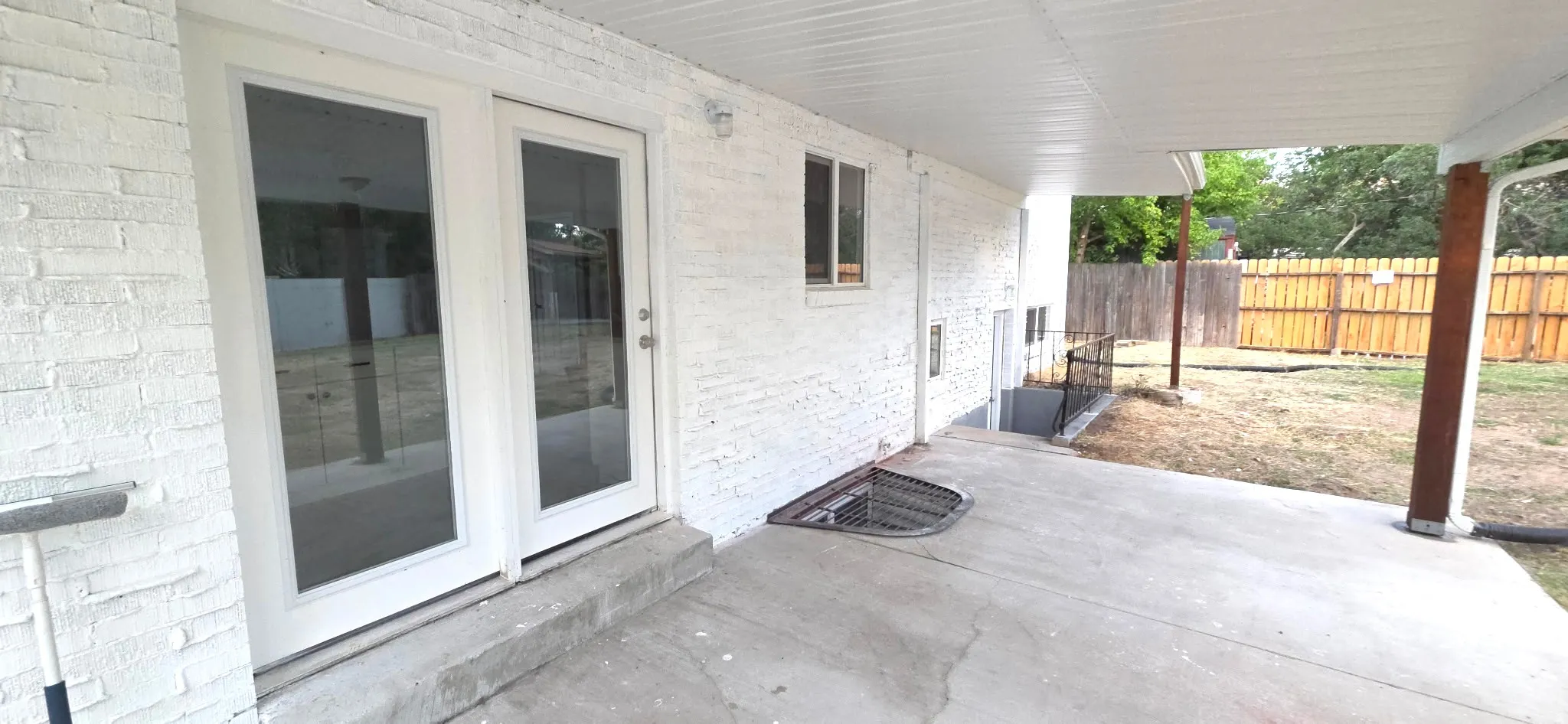 Covered patio with a concrete surface, white painted brick exterior, and full-light double doors