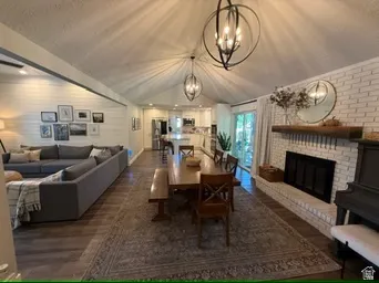 Vaulted ceiling with exposed beams, wood-finish flooring, white brick fireplace with mantel, recessed lighting, and modern orb chandeliers