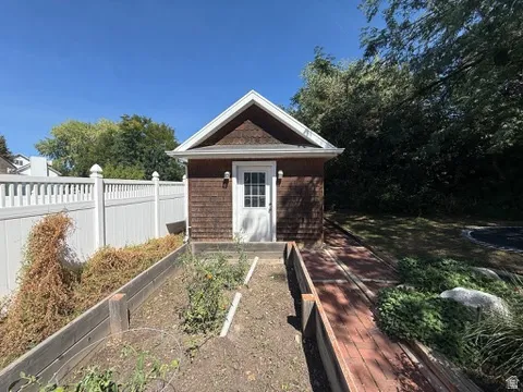 Shingle-sided outbuilding with white trim, a white door, and exterior lighting