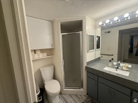 Bathroom featuring a shower enclosure, single vanity with a gray speckled countertop, white sink, and under-sink cabinetry