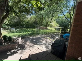 Expansive backyard featuring a manicured lawn, mature trees, and a paver patio with retaining walls