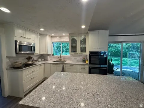 Kitchen featuring light-toned cabinetry, stainless steel appliances, a tile backsplash, recessed lighting, and a spacious island with a speckled countertop