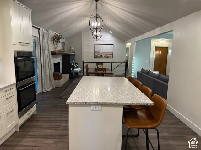 Vaulted ceiling with a contemporary chandelier, built-in double ovens, light-toned cabinetry, light-toned countertop, and wood-finish flooring