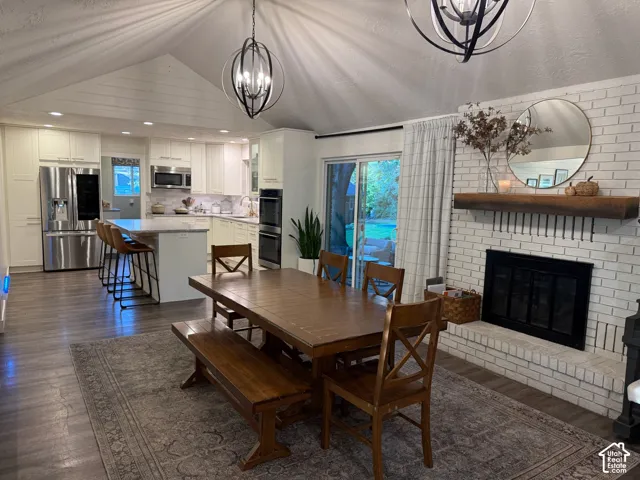 Vaulted ceiling with exposed beams, wood-finish flooring, white brick fireplace with wood mantel, built-in stainless steel double ovens, and sliding glass door