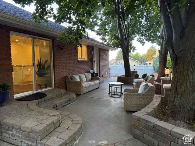 Expansive concrete patio featuring mature trees, a brick exterior, a sliding glass door, and paver stone retaining walls