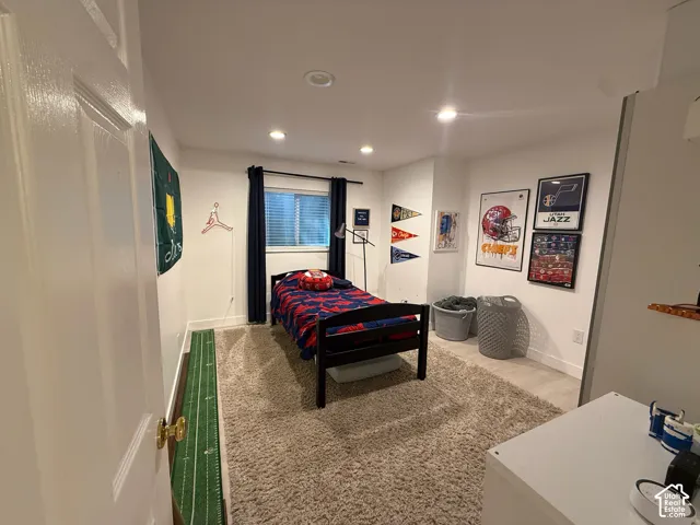 Recessed lighting illuminates a space featuring a window with blinds, carpeted flooring, and white walls