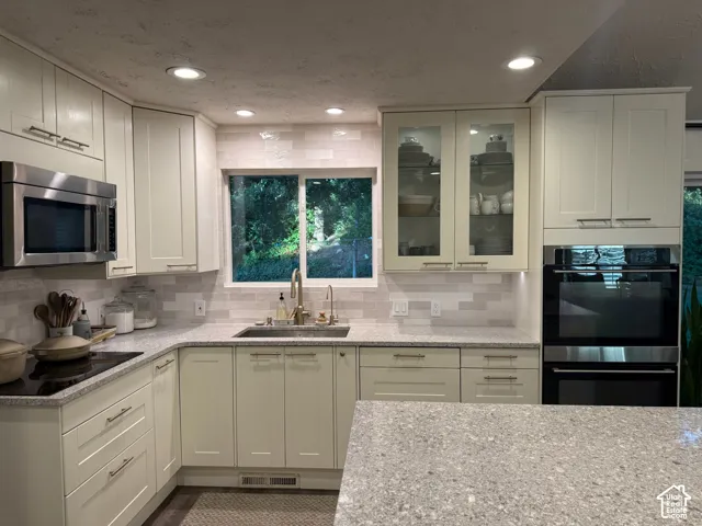 Integrated stainless steel microwave, built-in oven, light-toned cabinetry, subway tile backsplash, and speckled countertops