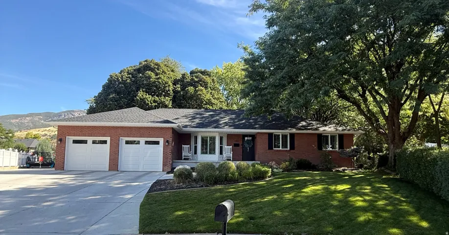 Brick exterior with a dual-car garage, mature trees, and a landscaped front yard