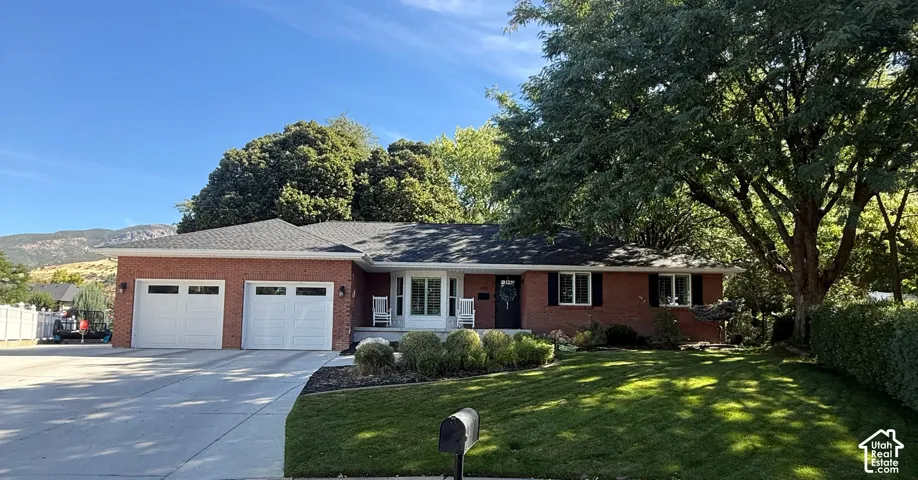 Brick exterior with white trim, two garage doors, a paved driveway, and established landscaping