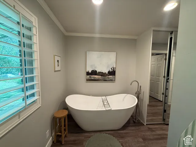 Freestanding soaking tub with a floor-mounted faucet, wood-finish flooring, recessed lighting, and crown molding