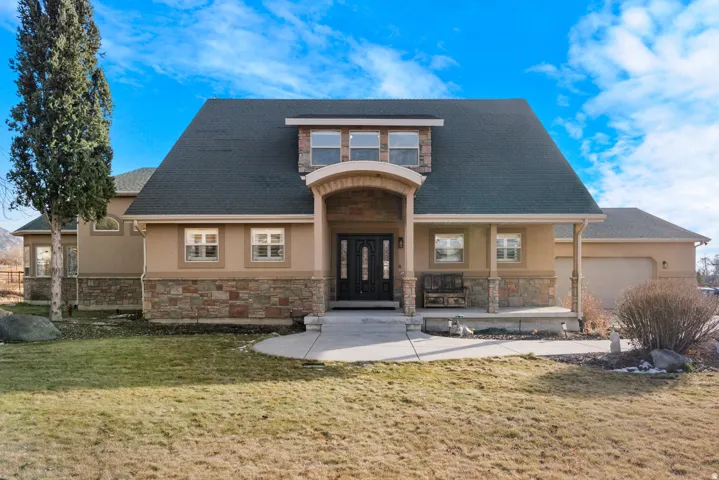 Stucco exterior with stone accent, arched entry, covered front porch, dormer window, and integrated garage