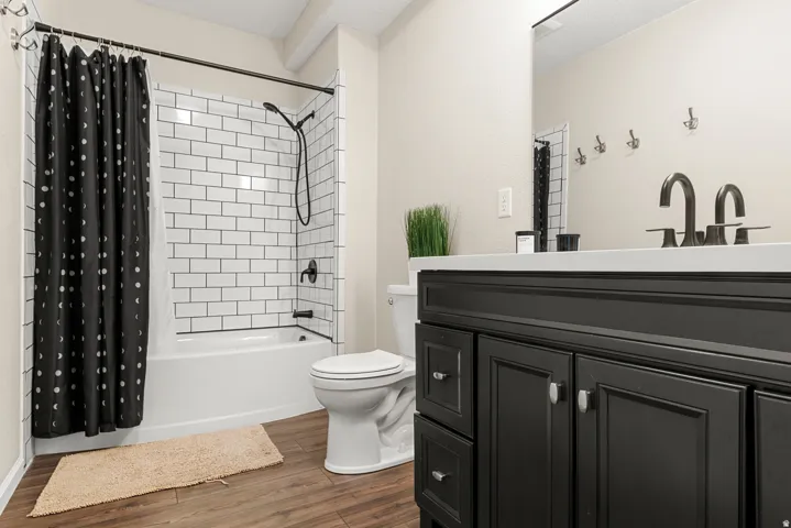White subway tile shower surround with a dark bronze shower fixture, white bathtub, and wood-finish flooring