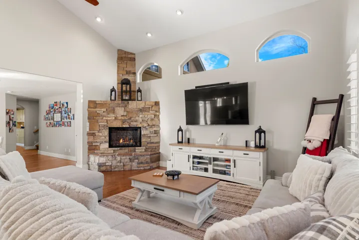 Vaulted ceiling, recessed lighting, stone-clad fireplace, wood-finish flooring, and arched window details