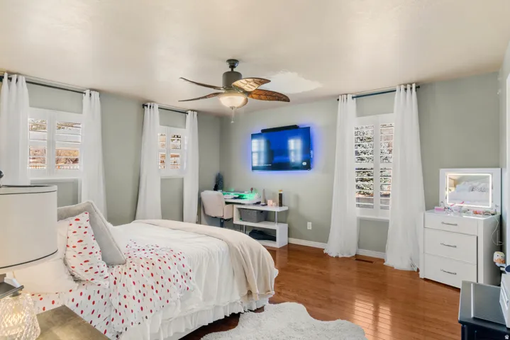 Hardwood flooring, multiple windows with white shutters, a ceiling fan with integrated lighting, and light gray wall paint