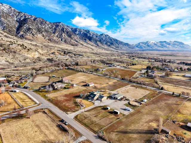 Expansive agricultural land with multiple structures and a circular fenced area, set against a mountainous backdrop