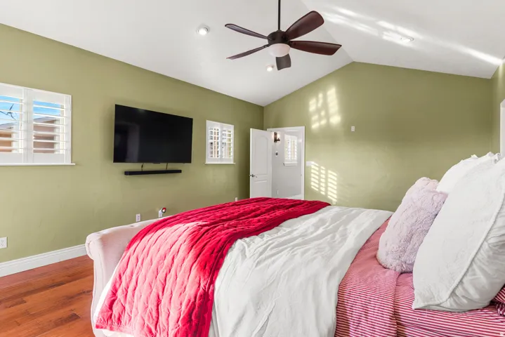 Vaulted ceiling with a ceiling fan, recessed lighting, wood-finish flooring, and white louvered shutters