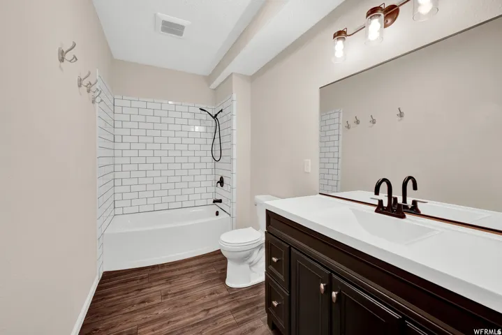 Tub and shower combination featuring subway tile surround, dark wood-finish vanity with white countertop, integrated sink, and an expansive wall-mounted mirror