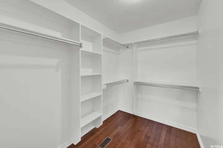 Hardwood flooring, built-in shelving, white walls, and multiple hanging rods provide storage