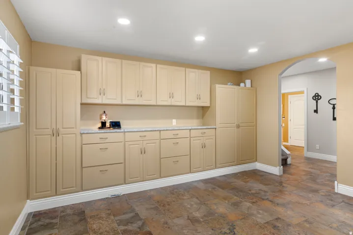 Built-in cabinetry with extensive storage, light-toned countertops, recessed lighting, arched entryway, and tile flooring
