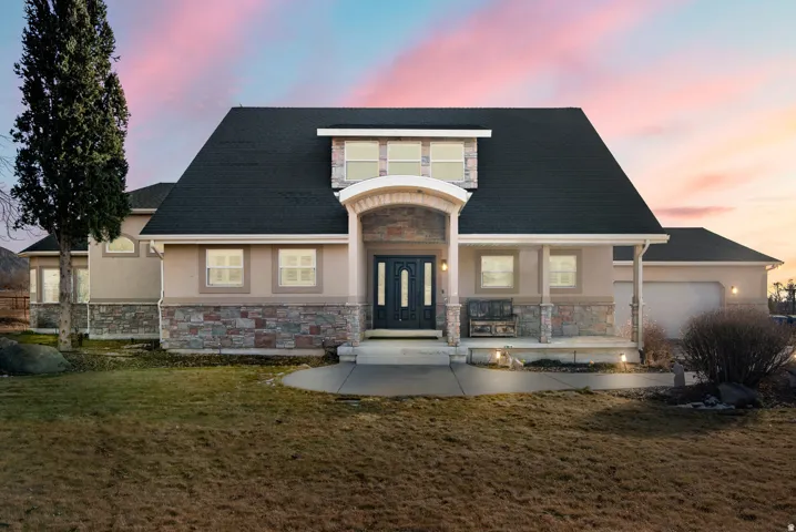 Stucco exterior with stone accenting, covered entry porch, dark shingle roof, and an attached garage