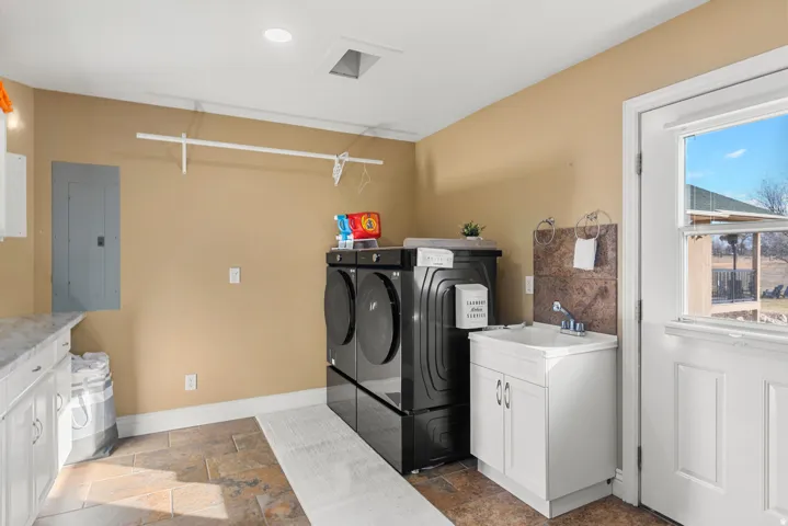 Tiled flooring, white cabinetry with a marble-finish countertop, a utility sink with a tiled backsplash, a window, and a built-in hanging rod