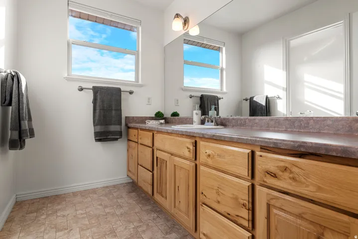 Bathroom vanity with light wood-finish cabinetry, integrated sink, and an expansive mirror