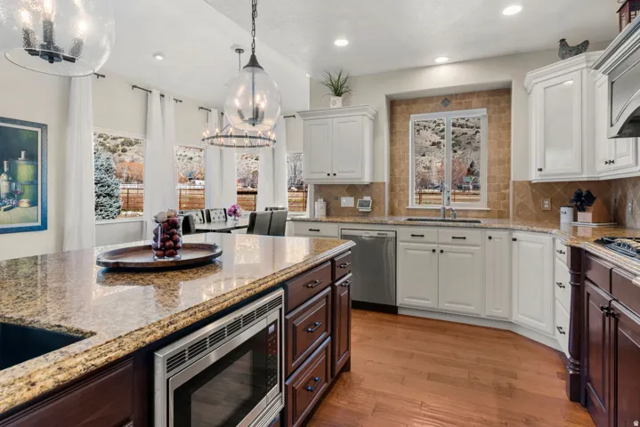 Kitchen featuring granite countertops, wood-finish flooring, white cabinetry, stainless steel appliances, and a tiled backsplash