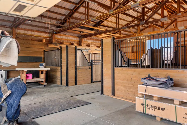 Barn interior featuring multiple stalls with wood-finish walls and metal grates, concrete flooring, and an exposed wood beam ceiling