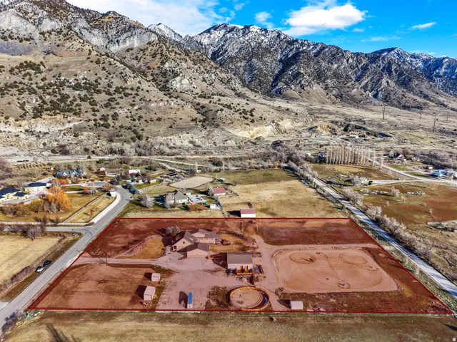 Expansive property featuring a prominent residence, several outbuildings, a riding arena, and a round pen, all set against a dramatic mountain backdrop