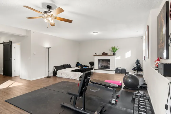 Spacious room featuring wood-finish flooring, a ceiling fan with integrated lighting, and a fireplace with a white tile surround