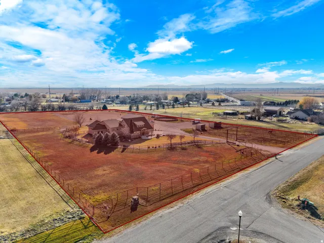 Expansive property featuring a large residence with a multi-gabled roofline, substantial fenced acreage, and clear skies