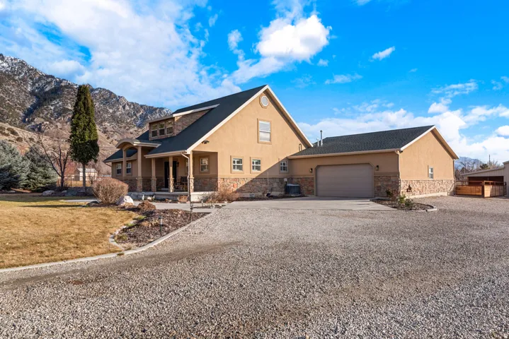 Stucco exterior with stone accents, attached garage, covered front porch, gravel driveway, and a mountain backdrop