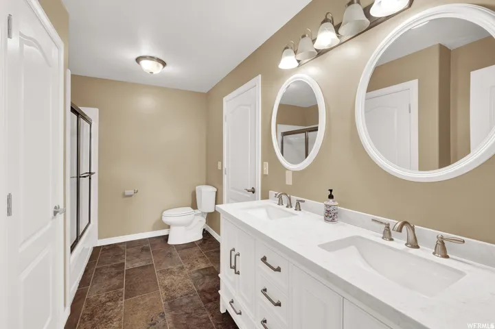 Dual vanity with undermount sinks and brushed nickel faucets, framed mirrors, enclosed shower, and tile flooring