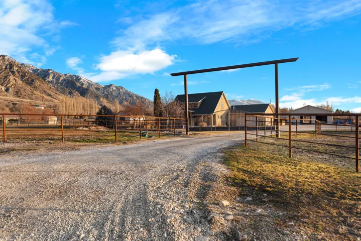 Gravel drive leading to a property entrance with metal fencing and a mountain backdrop