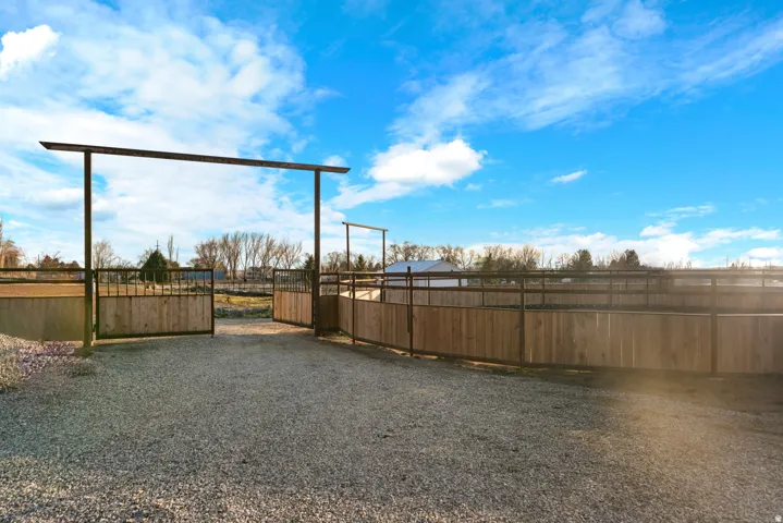Gravel drive with metal-framed gate, wood fencing, and open-air enclosure