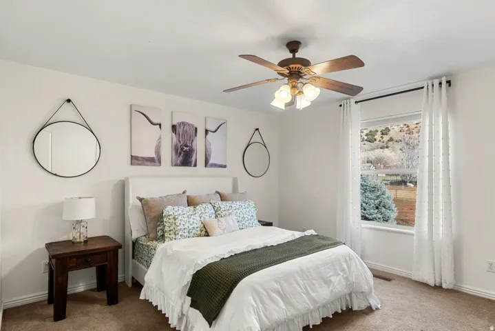 Window with mountain backdrop, ceiling fan with integrated lighting, wall-to-wall carpeting, and a neutral color palette