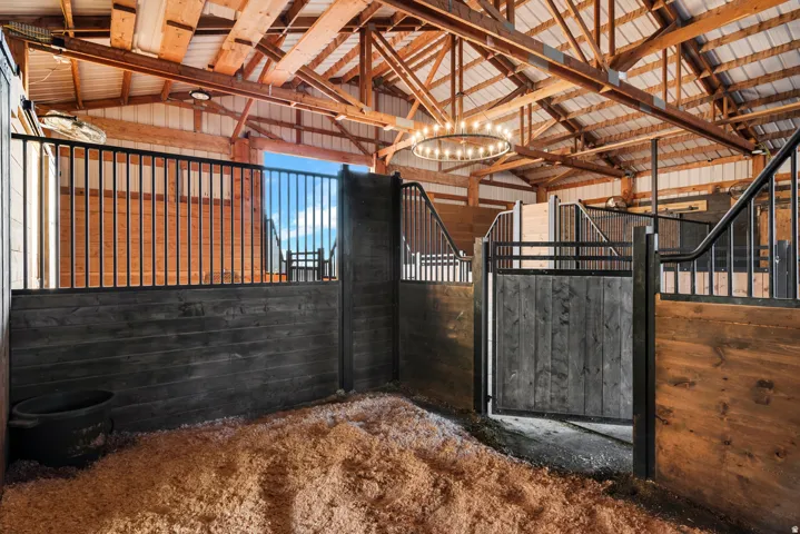 Exposed wood beam ceiling, metal roof, wood-paneled stalls, wrought iron gates, and a prominent circular chandelier