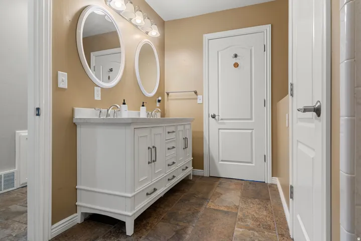 Double vanity with a light-toned countertop, dual oval mirrors, and a multi-bulb light fixture