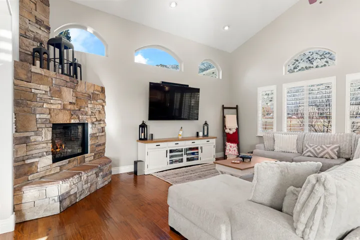 Sophisticated great room showcasing soaring ceilings with transom windows, a stacked-stone fireplace with integrated hearth, and hardwood flooring