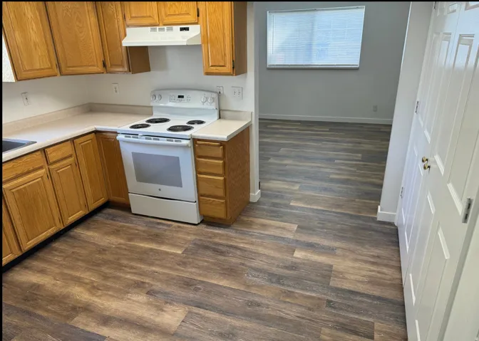 Kitchen featuring wood-finish flooring, wood cabinetry, white appliances, and light countertops