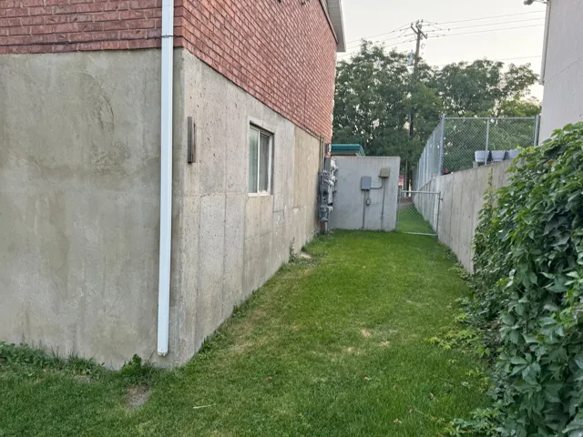 Brick exterior with stucco foundation, multiple utility meters, and a narrow grass pathway