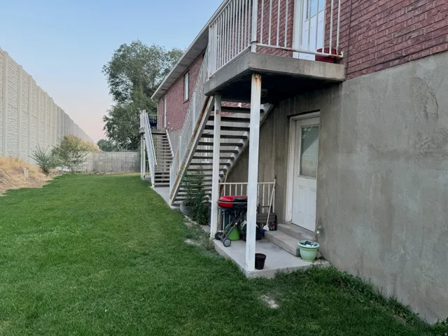 Expansive lawn area with a privacy fence, brick exterior, and two exterior staircases with metal railings