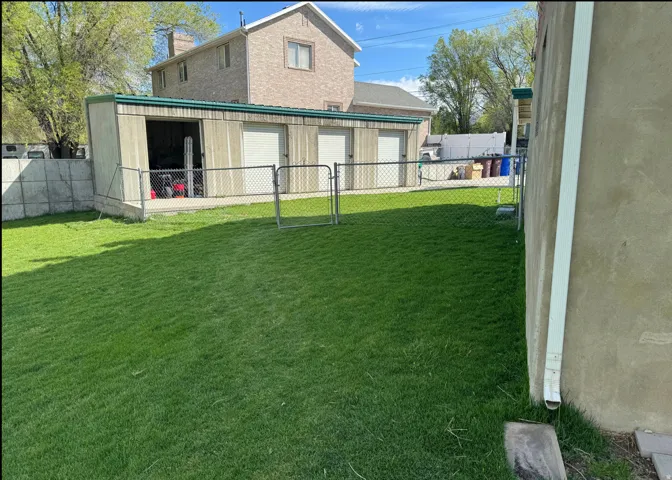 Expansive lawn area with a chain-link fence, concrete retaining wall, and an outbuilding featuring three garage doors