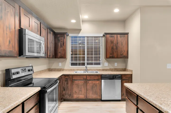 Kitchen featuring wood cabinetry, stone-finish countertops, stainless steel microwave, stainless steel dishwasher, and a double basin sink