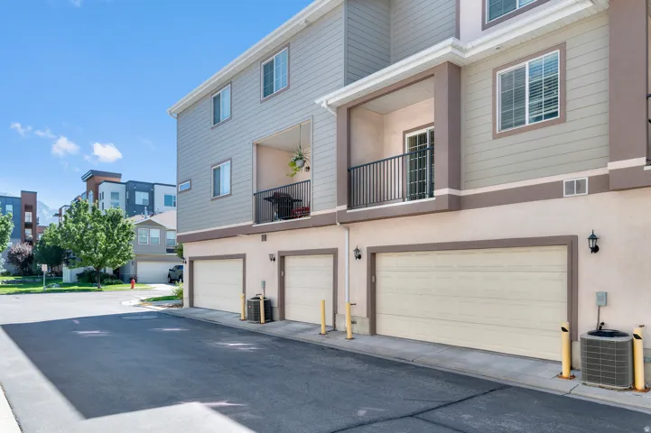 Multi-level building exterior featuring private balconies with black railings, individual garage doors, and stucco and siding finishes