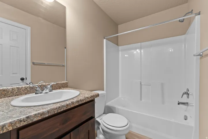 Bathroom with a wood-finish vanity, integrated sink, and a shower-tub combination with a white surround