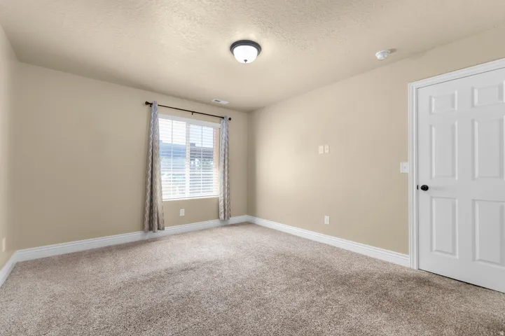 Neutral wall color, wall-to-wall carpeting, window with blinds, panel door with dark hardware, and overhead lighting fixture